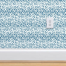 Load image into Gallery viewer, Wallpaper with blue dots of various sizes on a pale blue background on a mock wall with a baseboard and outlet plug
